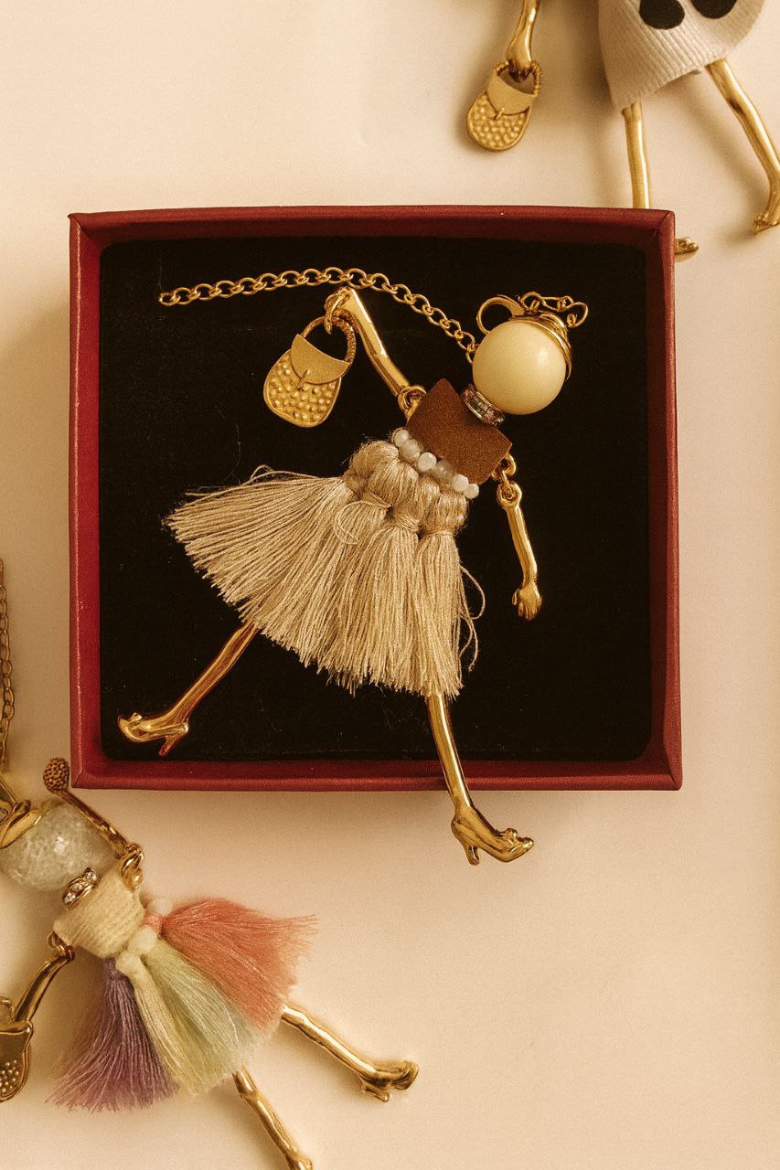 Muñequita Vainilla con faldita de flecos en crema y champagne — collar artesanal con sombrero de cuero y perlas, baño de oro 18K